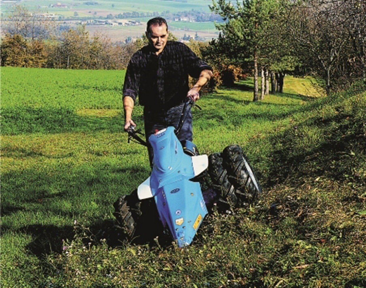ein Mann mäht an einem Hang den Rasen